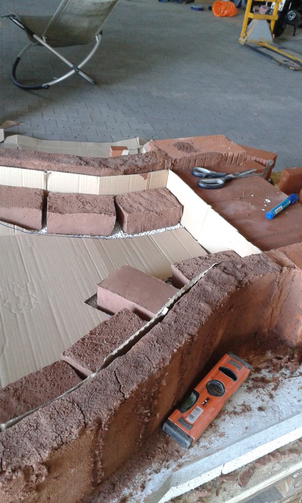 Dann noch eine Reihe liegend, und Du kannst mit der Kuppelwölbung beginnen. Auf die auf der Isolierung liegenden Ziegel kommt noch ca 2cm Dickbett Ton und die Biberschwänze, welche die Bodenplatte bilden. Also noch mal ca. 4cm. So viel halt, daß es eine ebene Fläche mit der "Einfahrt" bildet.